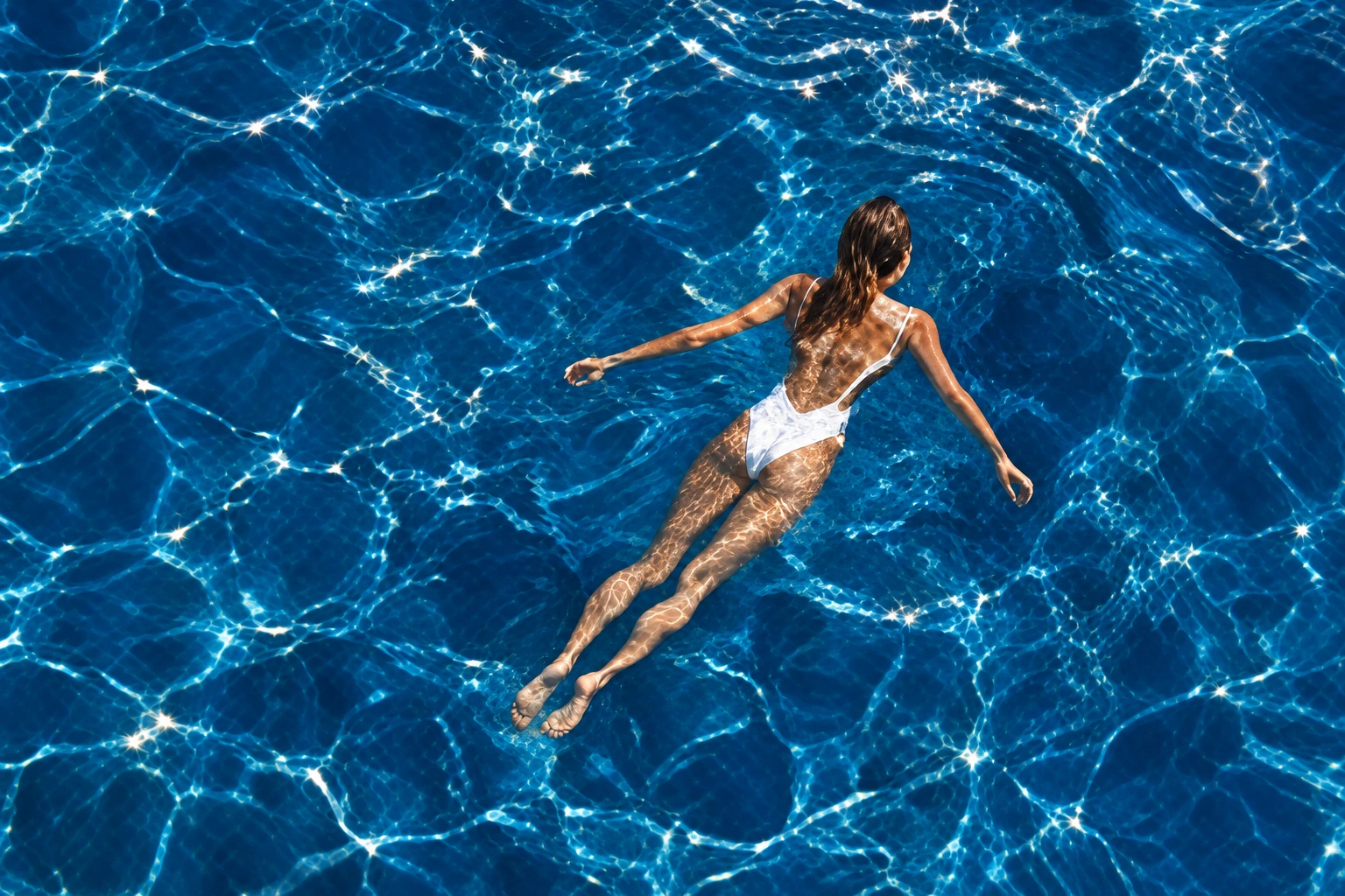 A woman floating in deep blue water, the visual mood of PHOS